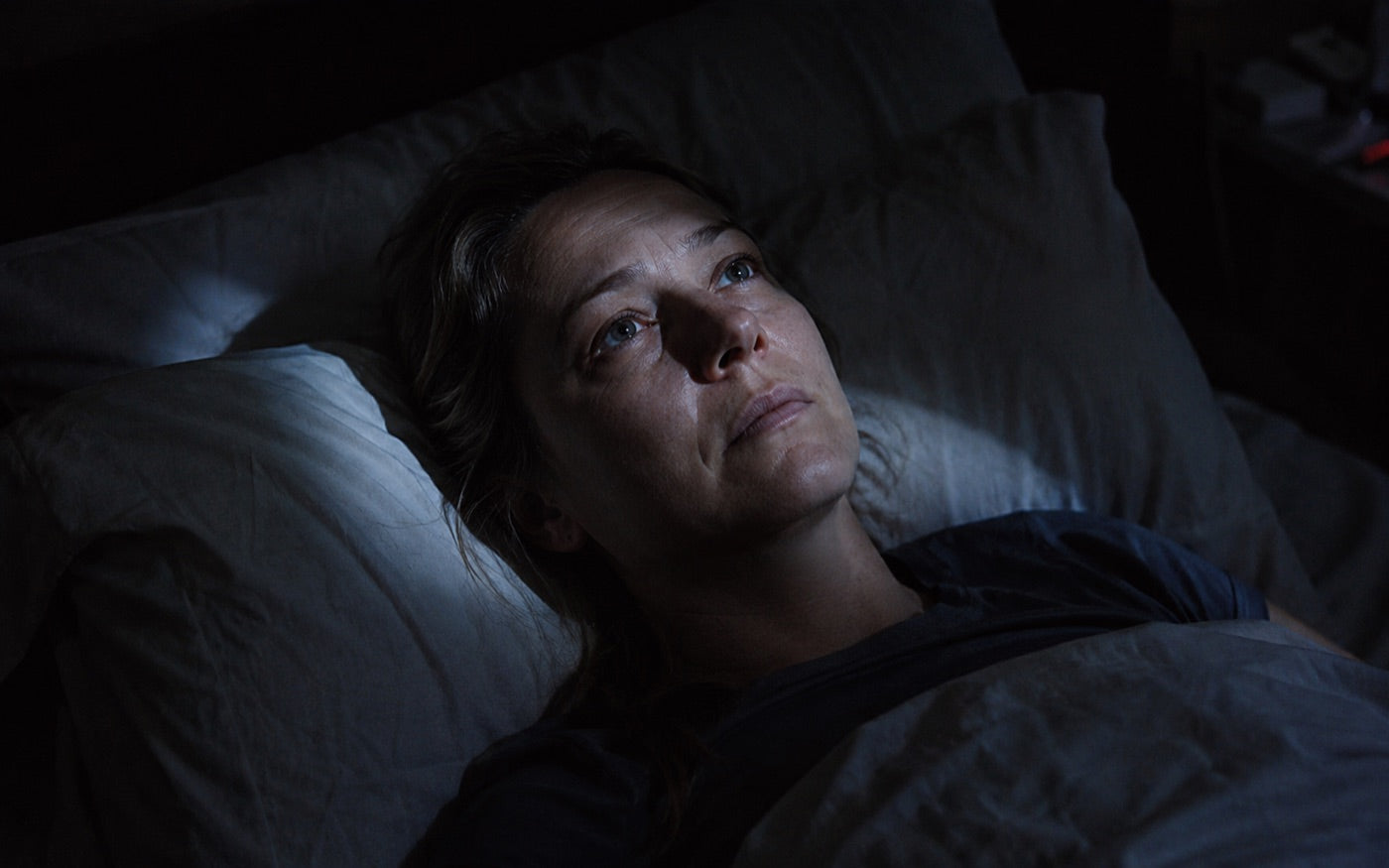 A woman lying awake in bed at night, eyes open, staring at the ceiling